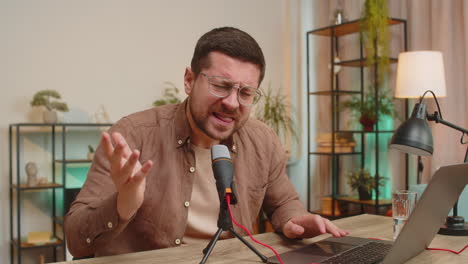 young positive caucasian man blogger singer using laptop while singing into microphone at table