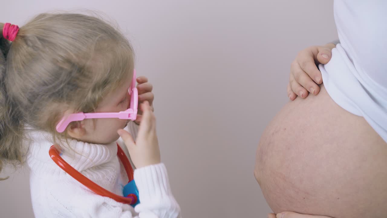 la ragazza con gli occhiali gioca al dottore con la mamma incinta nella stanza.