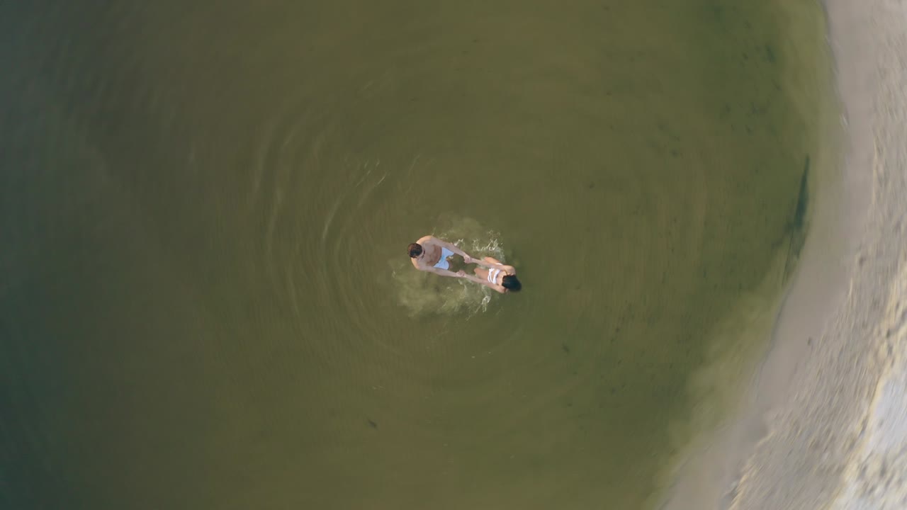 el hombre y la mujer tomados de la mano en círculo y girando en el agua