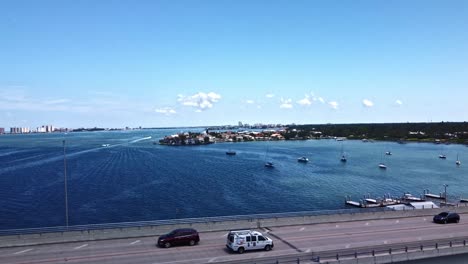 Die-Bellaire-Causeway-Bridge-In-Belleair-Beach,-Florida,-USA,-Hat-Viele-Autos,-Die-Auf-Beiden-Fahrspuren-Fahren,-Während-Sie-Von-Einem-Blauen-Meer-Und-Einer-Weit-Entfernten-Gemeinde-Flankiert-Wird