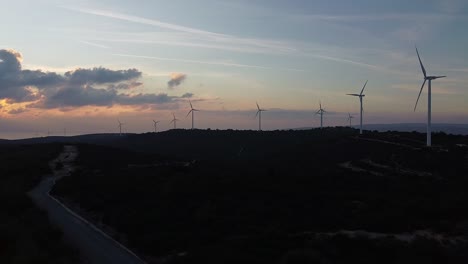 wide drone shot of wind turbines spinning against a beautiful orange sunset sky on a european countryside