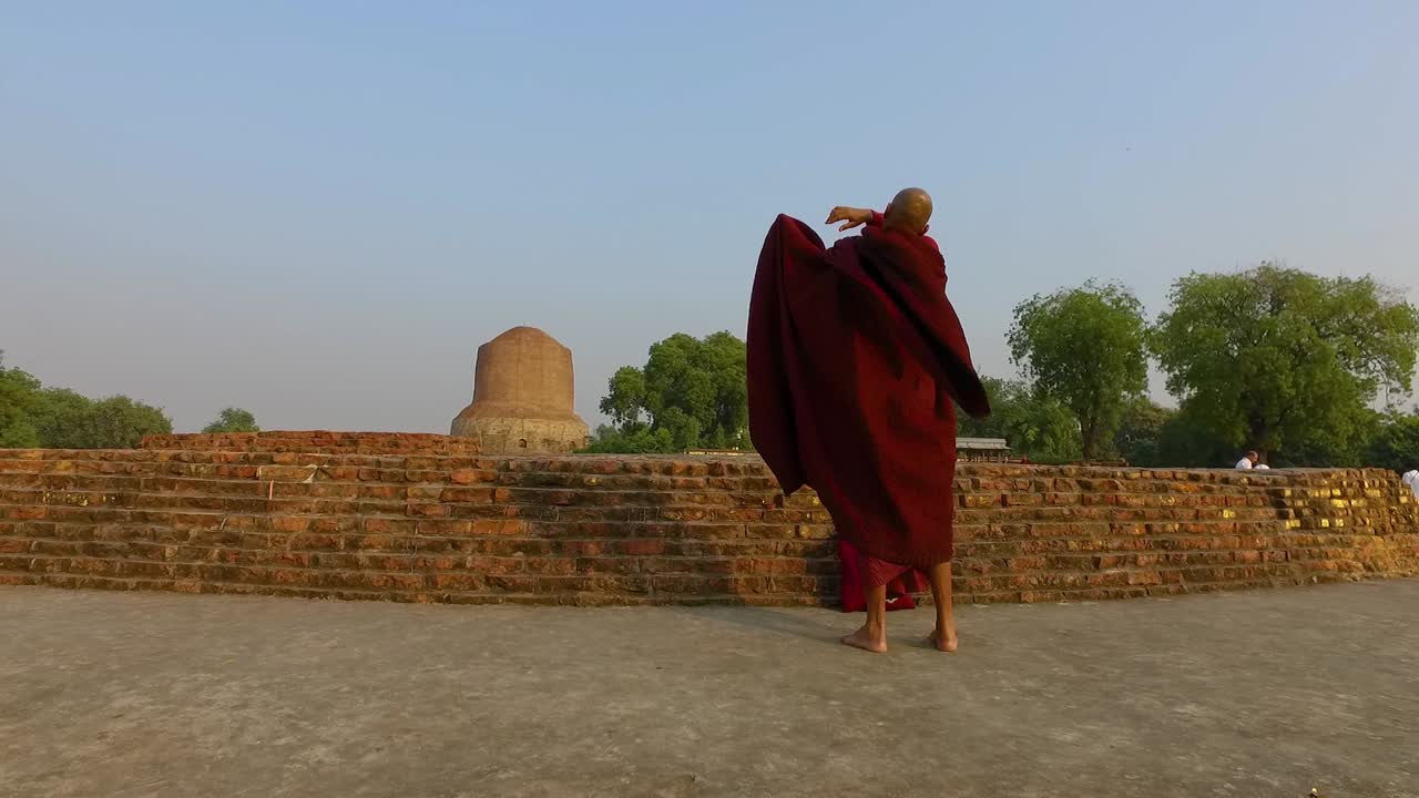 Un monaco buddista avvolge il suo Chivara con vista sullo Stupa di Dhamek a Varanasi, India