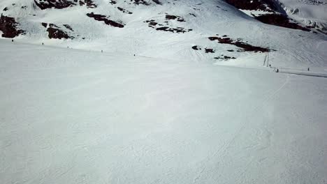 Drone-shot-of-a-snow-plain-in-the-swiss-alps-with-people-skiing-and-snowboarding-downhill