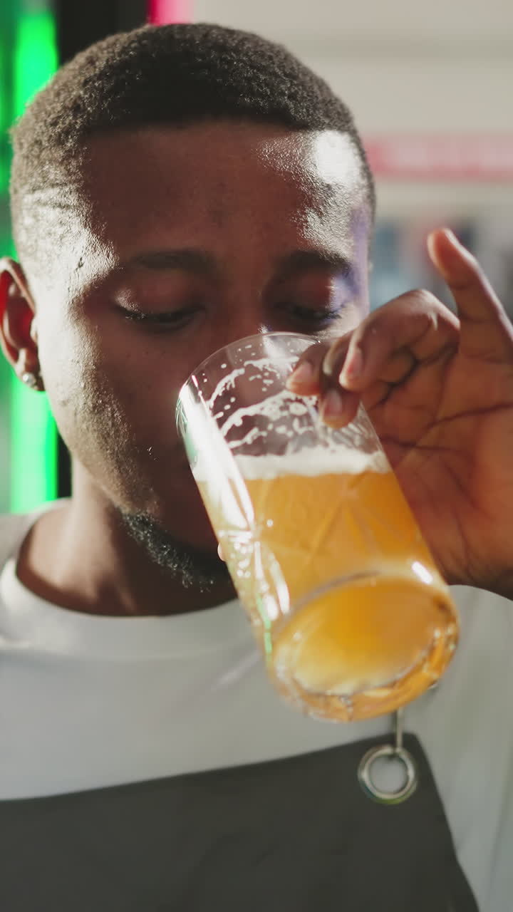 el sirviente bebe cerveza en el mostrador del pub. el camarero afroamericano degusta una bebida alcohólica espumosa descansando después de un duro trabajo en el bar. producto de cervecería artesanal