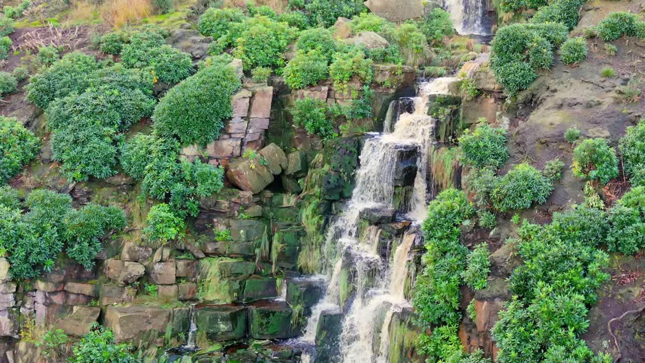 Yorkshire moor's enchanting waterfall, aerial shot: water flows over boulders, dropping into a deep blue pool, with hikers around