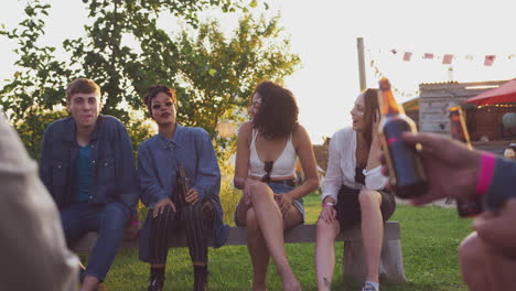 group of young friends at music festival sitting around fire and drinking beer