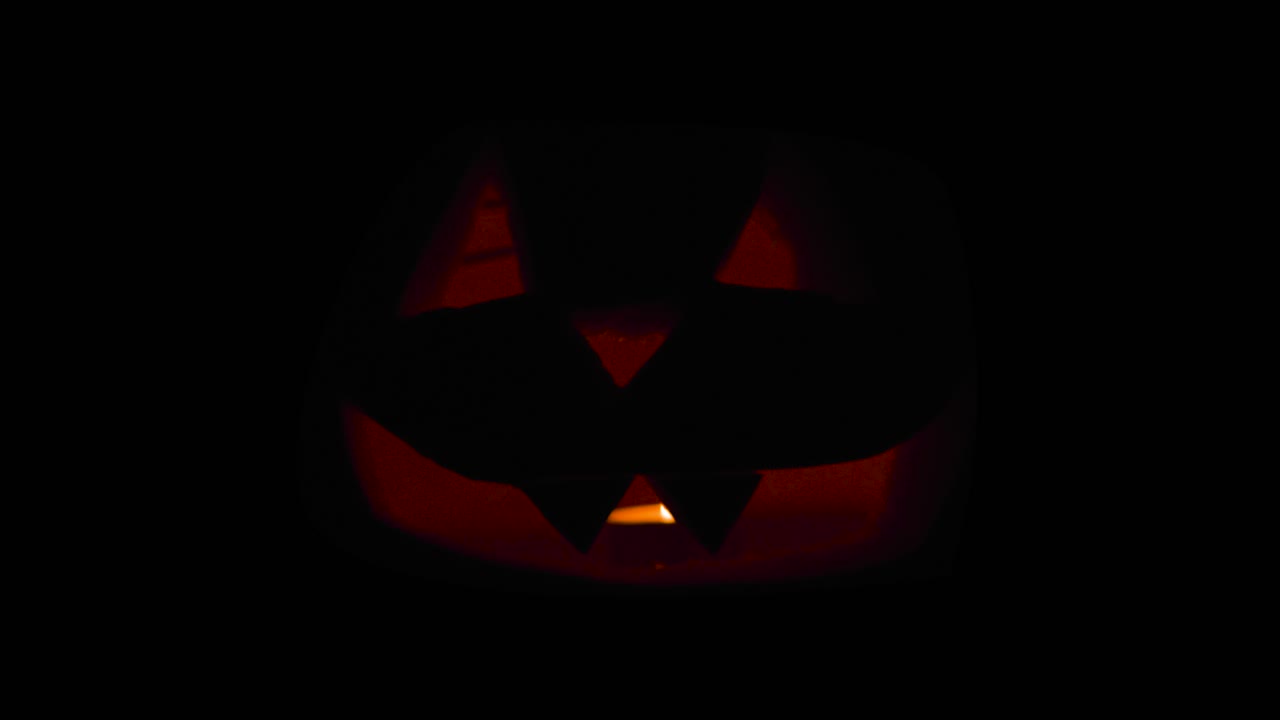 Happy Halloween Creepy Jack O' Lanterns glowing in the dark wishing Happy Halloween: carved Pumpkin decorations with burning candles inside.