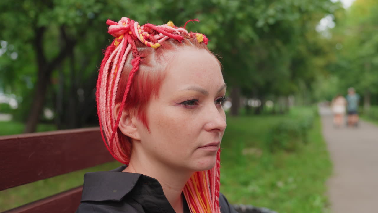 평온한 공원 풍경, 핑크색 땋은 머리를 한 여성이 평화롭게 쉬고 있어요. 조용한 여성이 공원 벤치에 앉아 주변을 관찰하고 있으며, 평화로운 공원 환경에서 핑크색 땋은 머리를 한 여성의 고요한 순간을 담았습니다.