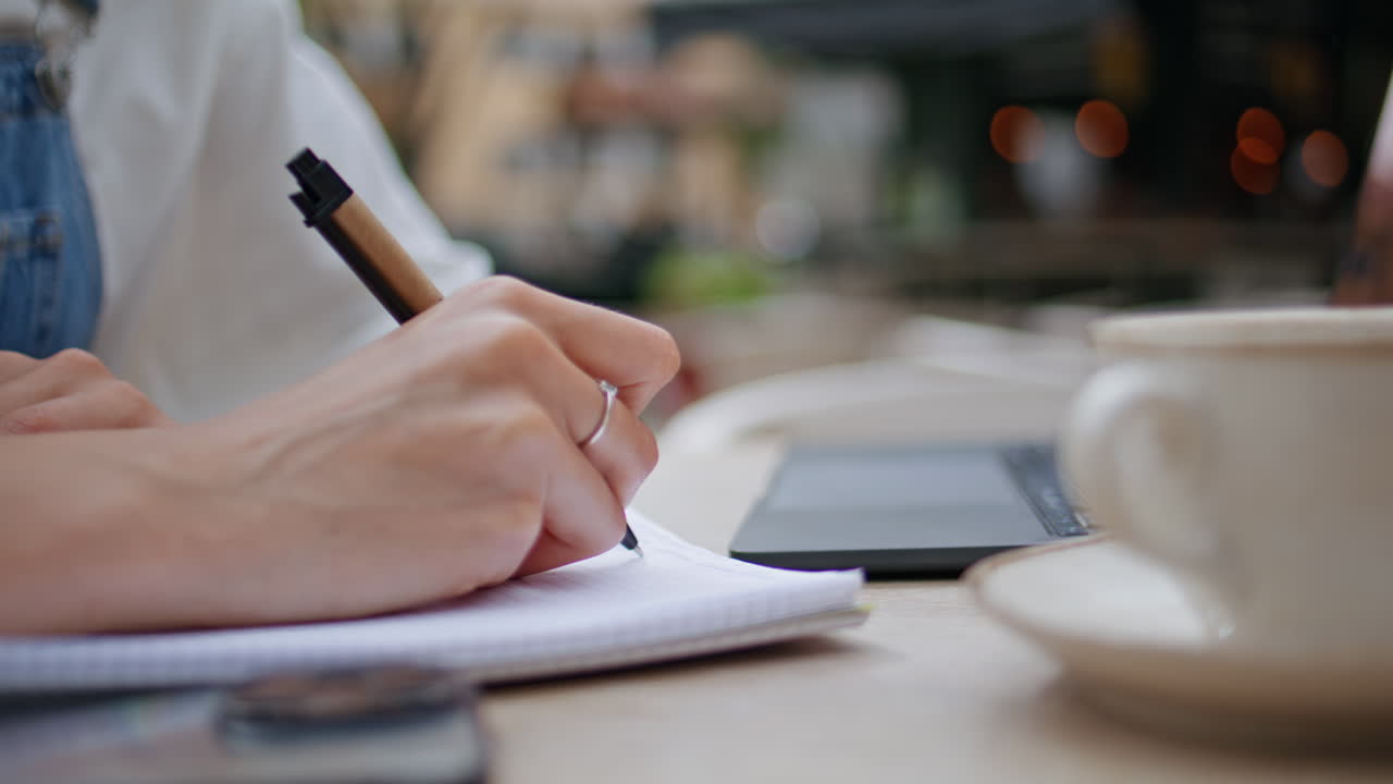 Woman hand writing notebook at outdoors cafe closeup. Unknown female writer