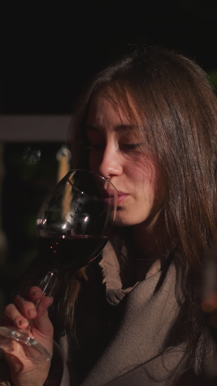 Woman tastes wine with friend on night terrace. Young couple spends first romantic date in cozy restaurant. Pretty lady rests with boyfriend