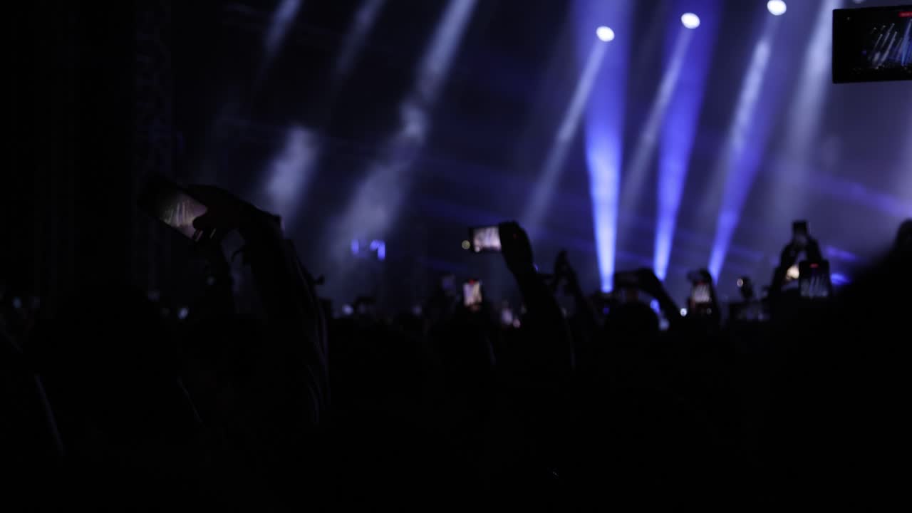 I fan riprendono filmati del concerto dal vivo con gli smartphone mentre il cantante si esibisce su un palco illuminato