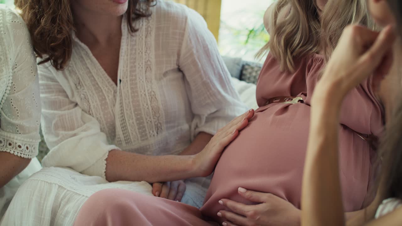 Nedre del av en gruppe voksne kvinner på en babyshower som berører magen til en gravid kvinne