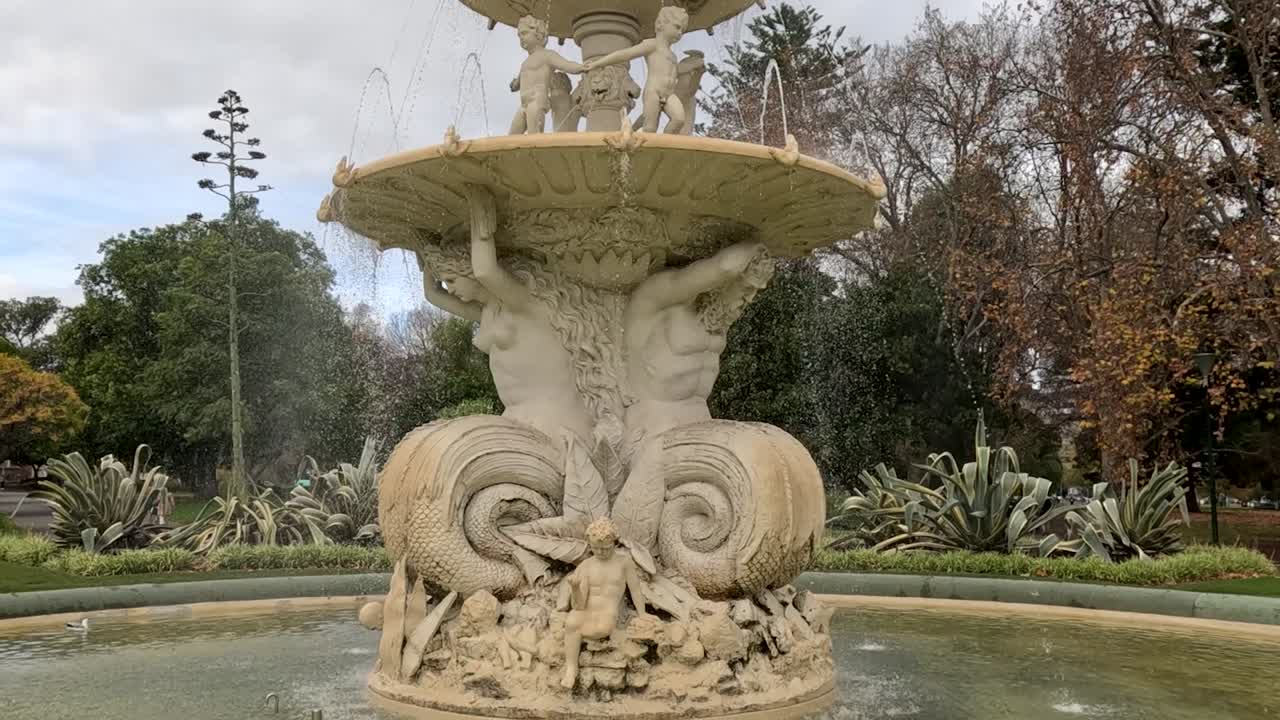 A detailed view of a multi-tiered fountain adorned with sculptures, surrounded by lush greenery and trees.
