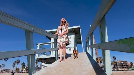 Hermosa-Joven-Rubia-Y-Lindo-Perro-Caminan-Por-Una-Rampa-De-La-Estación-De-Salvavidas-En-La-Playa-De-Venecia-En-Cámara-Lenta