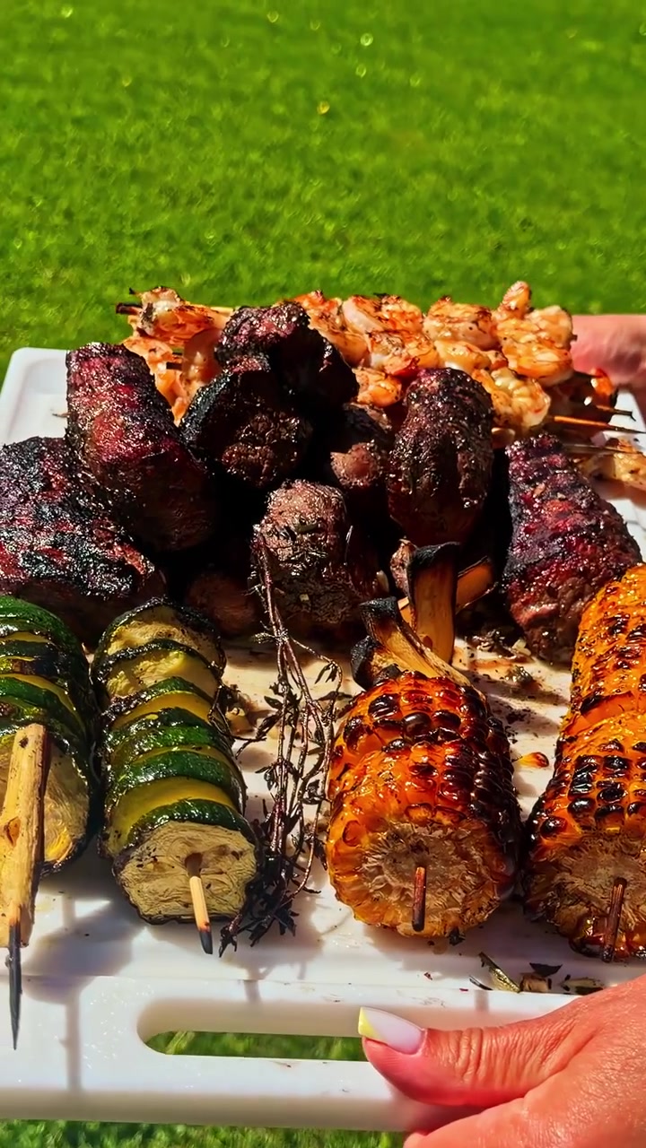 Persona che serve spiedini di manzo alla griglia accompagnati da pannocchie di mais carbonizzate e zucchine. - Scatto verticale