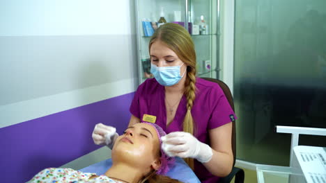 beautician cleans woman's face before a cosmetic procedure with napkins. video from the top.