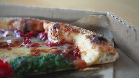 closeup shot of tasty neapolitan pizza with pesto sauce in a cardboard pizza box on the table, sliding shot