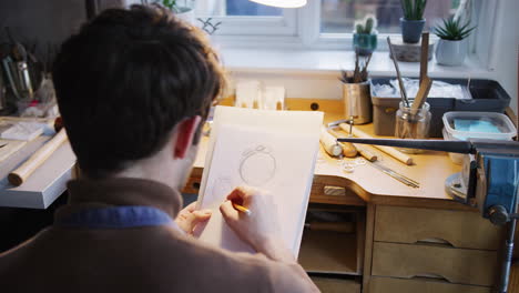 close up of male jeweller sketching out design for ring in studio