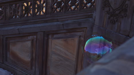 big soap bubble, ball shape floating in air next to building, moving dragged by breeze, fragile light colorful transparent shape flying