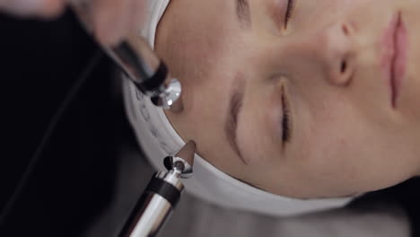 la doctora esteticista hace a la mujer micro corrientes terapia facial usando impulsos eléctricos en el salón de spa