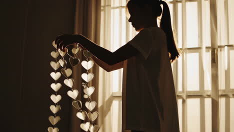 silhouette of a girl holding a string of heart decorations by a window