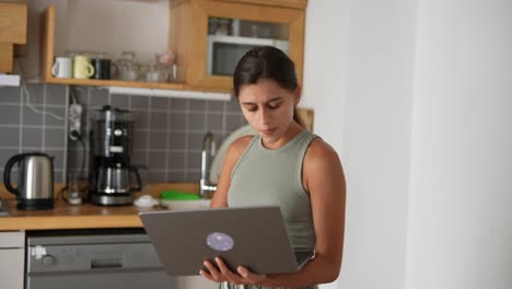 mujer joven trabajando en una computadora portátil en la cocina