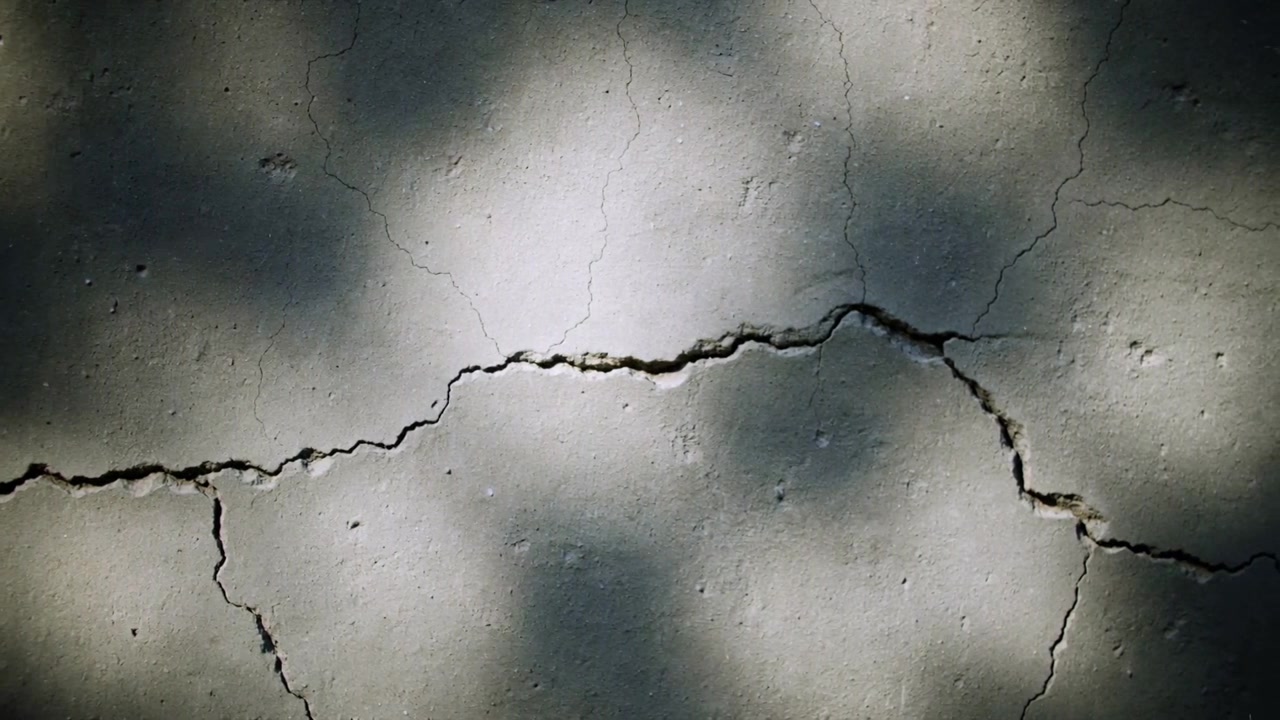 Shifting dappled sunlight drifting across main crack on pavement under trees, revealing fine cracks