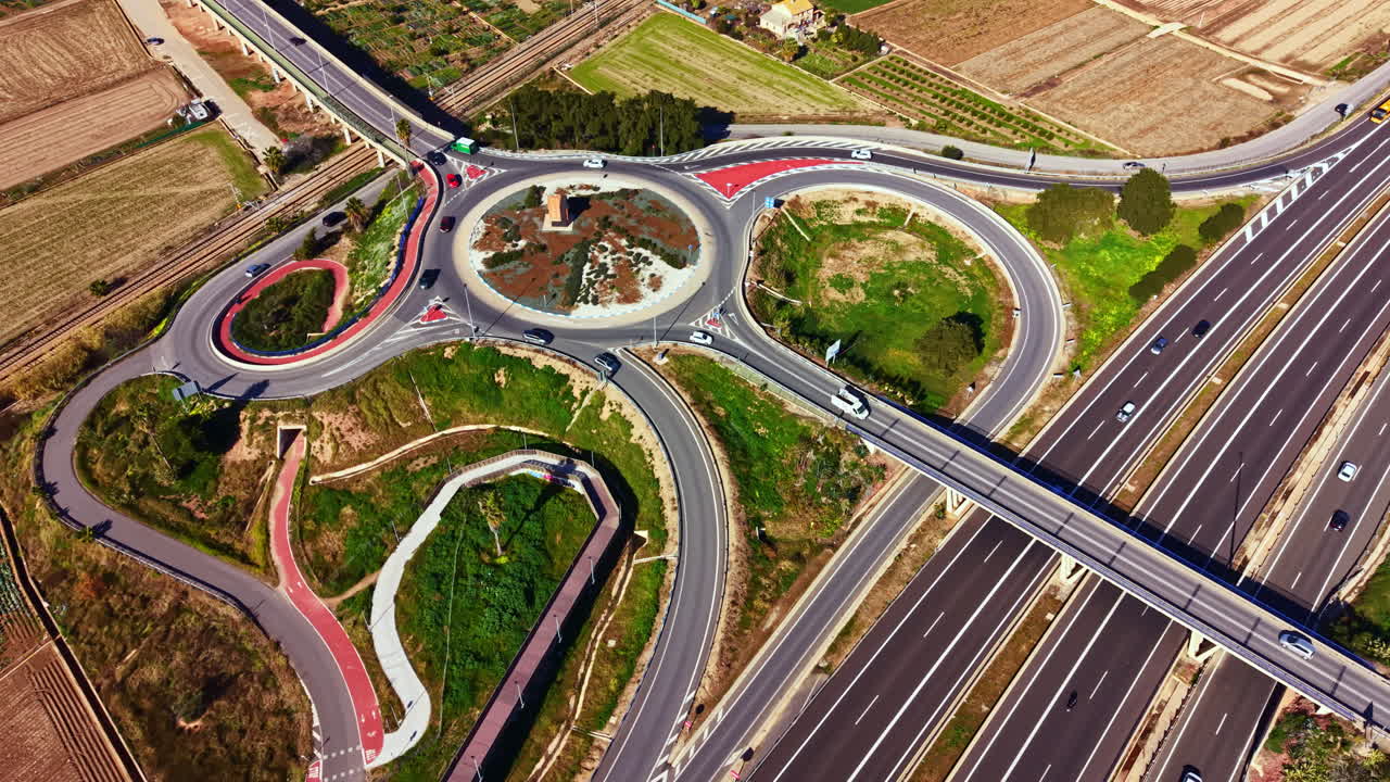 晴れた日、畑や道路が広がる田園地帯の高速道路近くにある円形交差点周辺を交通が流れています。