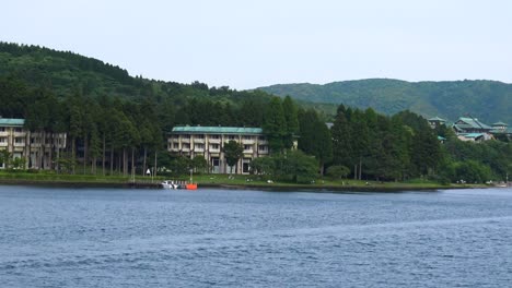 The-view-of-Ashi-lake-and-some-buildings,-with-a-motorboat-passing-by