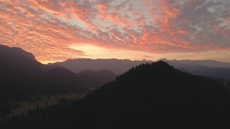silhouette of mountain ranges around beautiful valley under dramatic sky during golden hour. rising aerial.