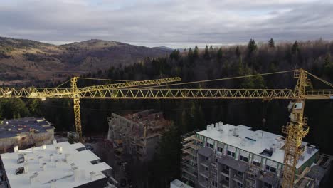 Vista-Aérea-De-Grúas-En-Un-Sitio-De-Construcción-En-Una-Montaña-Cubierta-De-Bosque