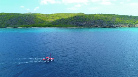 High-angle-static-aerial-view-of-fishing-boat-crossing-sea-with-rolling-hillside-rocky-coastline-behind