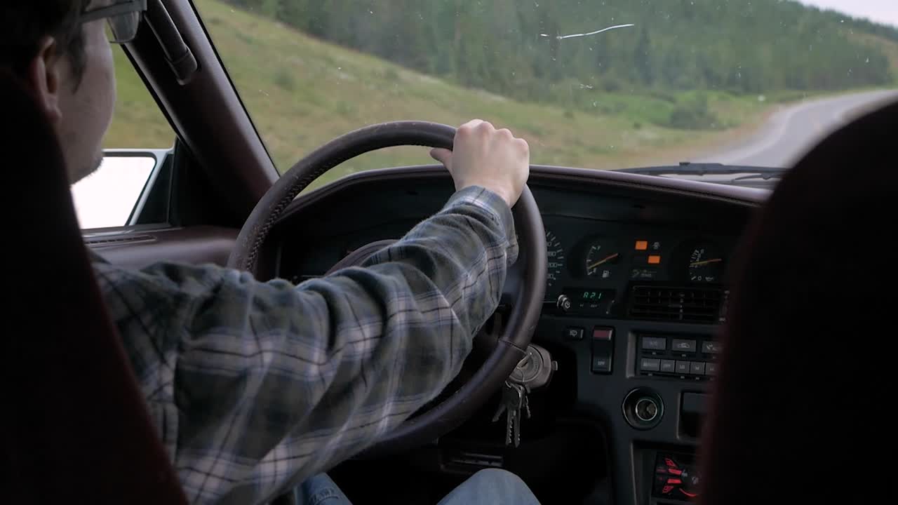 se ve a un hombre conduciendo un automóvil por una carretera con curvas a través de las montañas