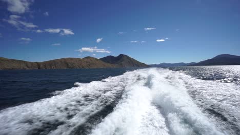 Cámara-Lenta---Parte-Trasera-De-Las-Olas-Del-Barco-Con-Cielo-Azul-Y-Montañas-En-Segundo-Plano