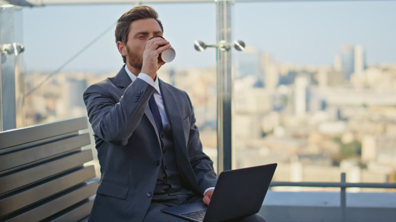 Confident executive sipping coffee on glass terrace. Handsome business browsing