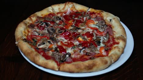 A close-up shot of a loaded pizza on a white plate, featuring a thick crust topped with tomato sauce, melted cheese, sausage, mushrooms, peppers, and onions.