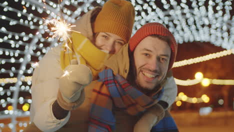 portrait of joyous couple with christmas sparkler outdoors