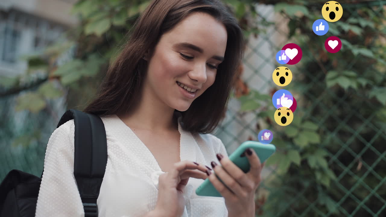 Young woman interacting with social media on her smartphone with floating reaction emojis