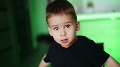 dark-haired caucasian boy in black t-shirt sitting on the chair. mom's hand gives a full spoon to her baby. blurred backdrop.