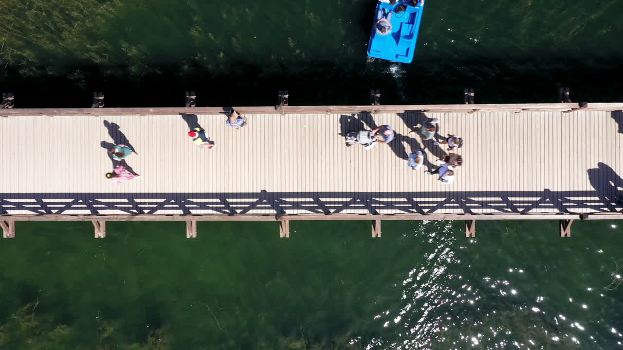 공중:배경에서 볼 수 있는 녹색 호수 물과 함께 트라카이의 나무 다리를 건너는 사람과 관광객의 조감도