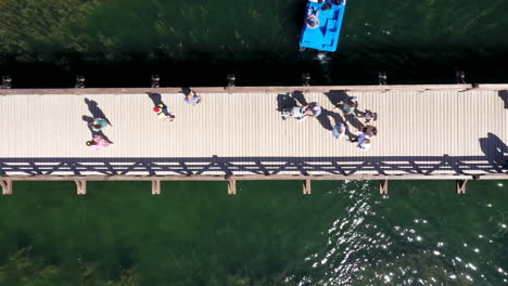 AERIAL:-Birds-Eye-View-of-People-and-Tourists-Walking-Across-Wooden-Bridge-in-Trakai-with-Green-Color-Lake-Water-Visible-in-the-Background