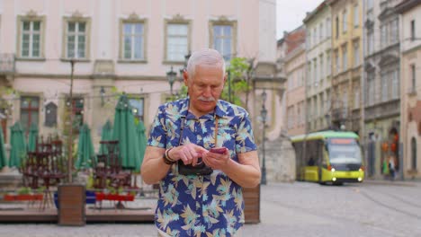 Anciano-Turista-Elegante-Que-Busca-La-Manera-De-Encontrar-Una-Ruta-Usando-Un-Teléfono-Inteligente-En-El-Casco-Antiguo-De-Lviv,-Ucrania