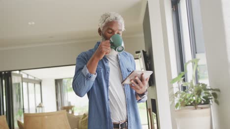 Video-of-african-american-senior-man-drinking-coffee-and-using-tablet