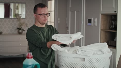 caucasian adult caucasian man with down syndrome folding the laundry