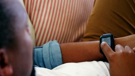 man lying on sofa and using smart watch in living room