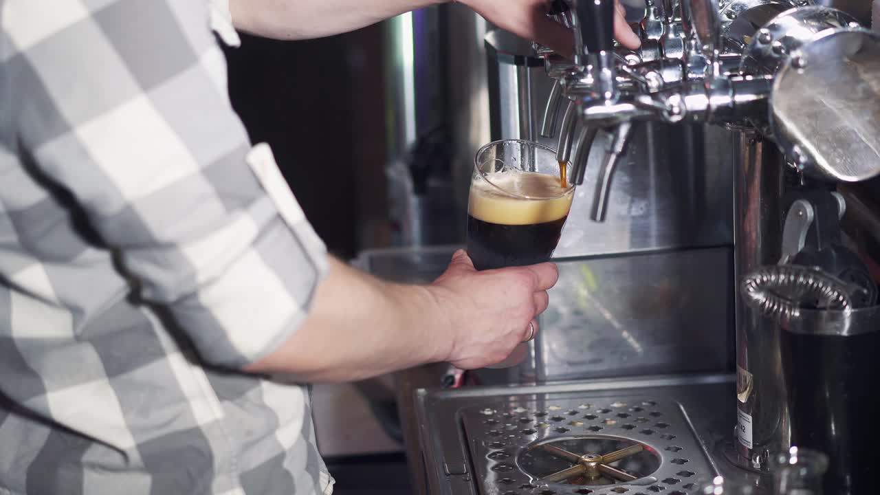 Barman pours dark beer into a glass from the beer tap in the pub. Bartender pouring perfect beer for client