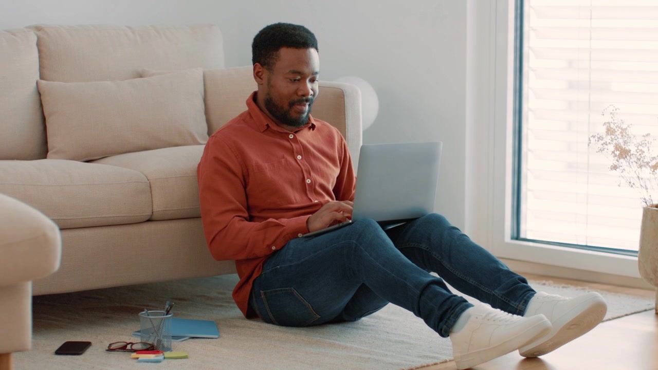Young Man Working on Laptop While Sitting on Living Room Floor