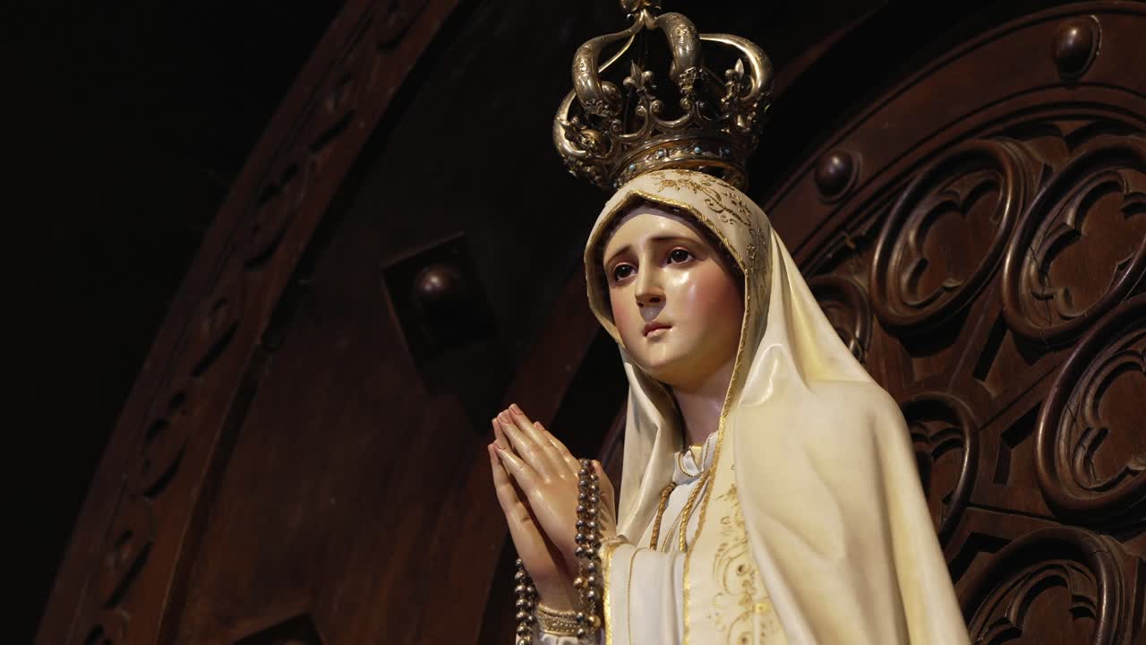 Elegant statue of Virgin Mary in prayer with a golden crown and rosary