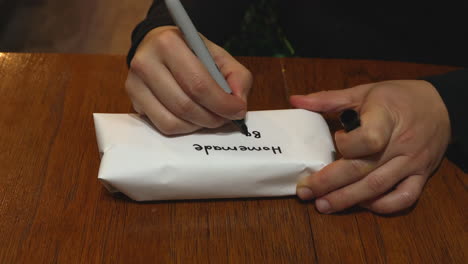 woman's hands writing label on white paper covering of homemade bacon in container