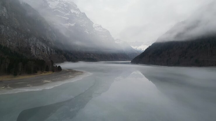 Klöntalersee Glarus Svizzera, volo a bassa quota sopra un incredibile lago ghiacciato con nuvole nebbiose.